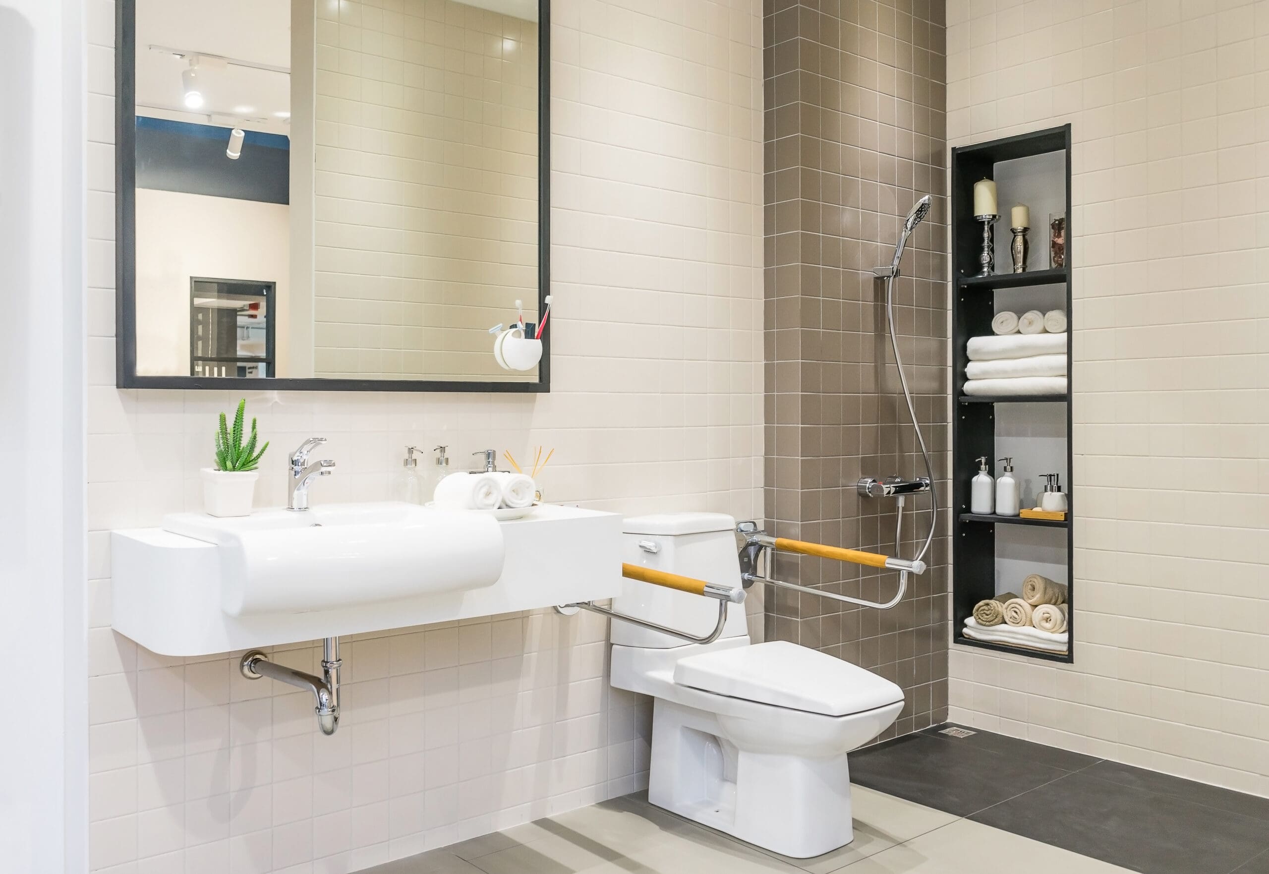 Modern accessible bathroom with disabled adaptations features a large sink, mirror, and a toilet equipped with grab bars. A built-in shelf stores towels and toiletries, while the clean, minimal decor enhances comfort for all abilities.
