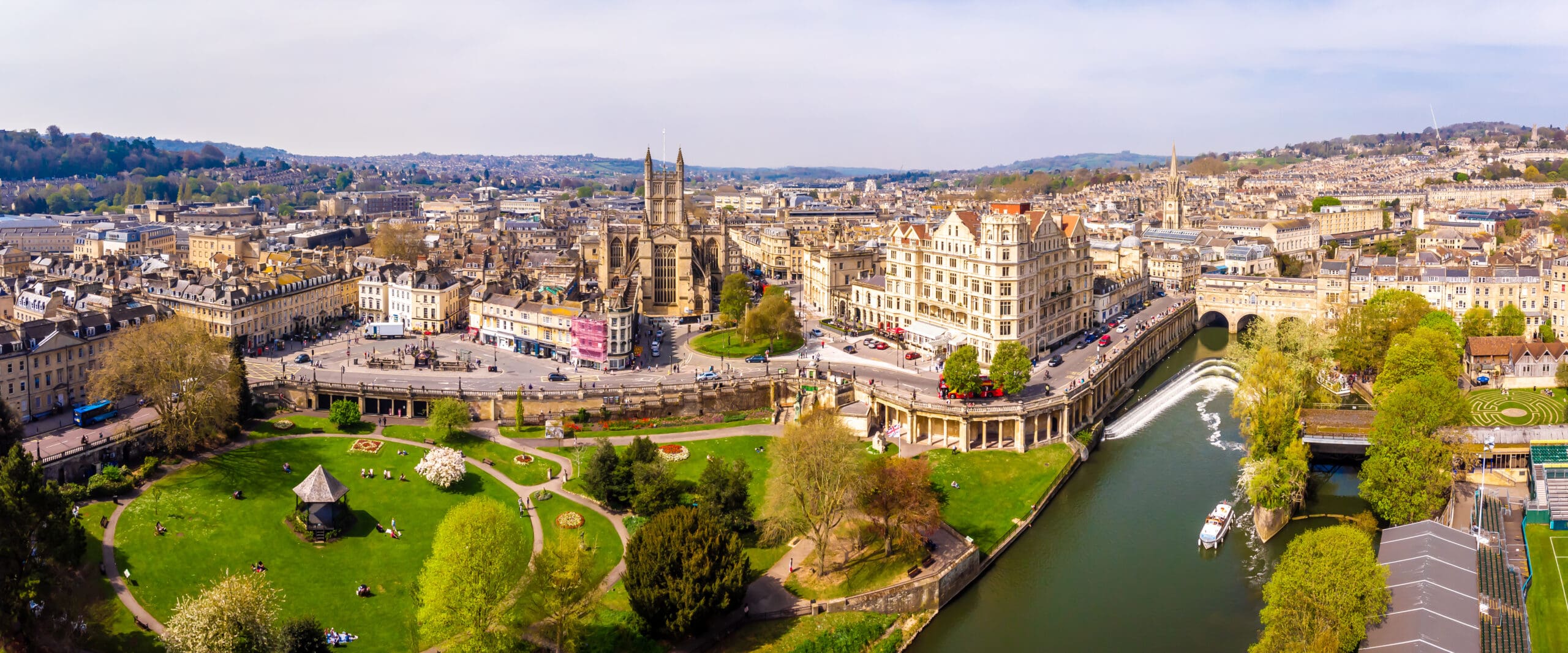 A panoramic aerial view of Bath, England, showing historic buildings, Bath Abbey, the River Avon with a weir, Pulteney Bridge, and green parks under a clear sky—where elegant homes feature modern kitchen installations and thoughtful disabled adaptations.