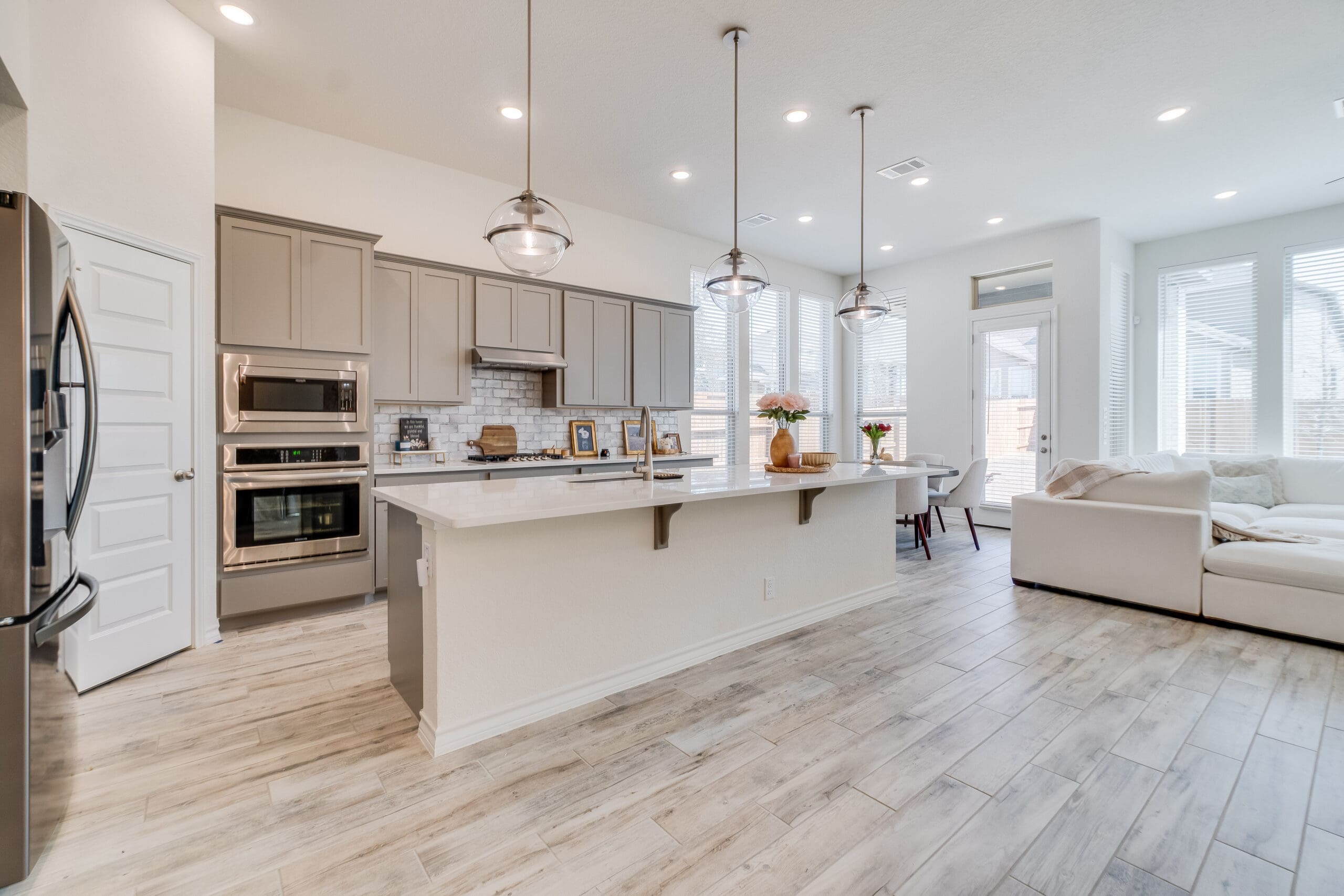 Modern open-concept kitchen and living area with light wood flooring, large island with sink, beige cabinets, stainless steel appliances, pendant lights, and bright windows—ideal for Kitchen Installations or Property Refurbishments.