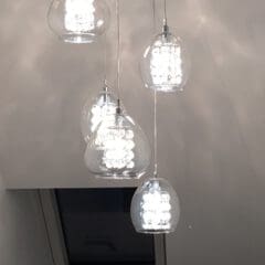 Five modern pendant lights with clear glass shades hang from the ceiling, glowing brightly. A rectangular window is partially visible below the lights—an elegant touch for kitchen installations or property refurbishments in contemporary homes.