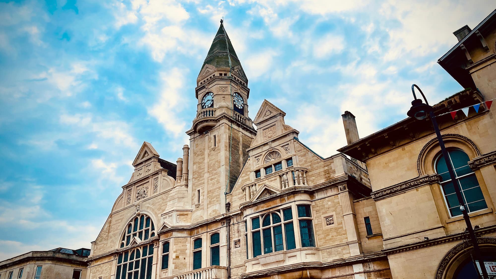 A historic stone building with a tall clock tower, arched windows, and ornate architectural details under a partly cloudy sky.